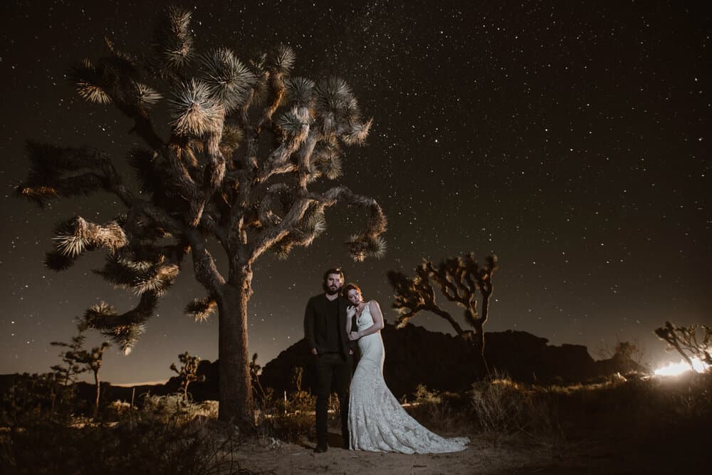 A bride leans on her groom standing in Joshua Tree at night.