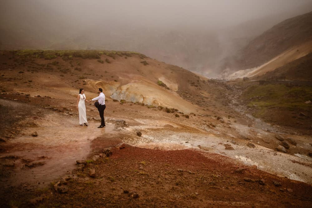 A man and woman hold each others hands on their elopement day as they wonder around the Iceland hot lands.