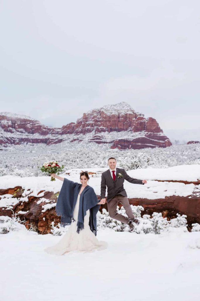 A couple jumps and smiles in the snow on a winter day in Sedona. 