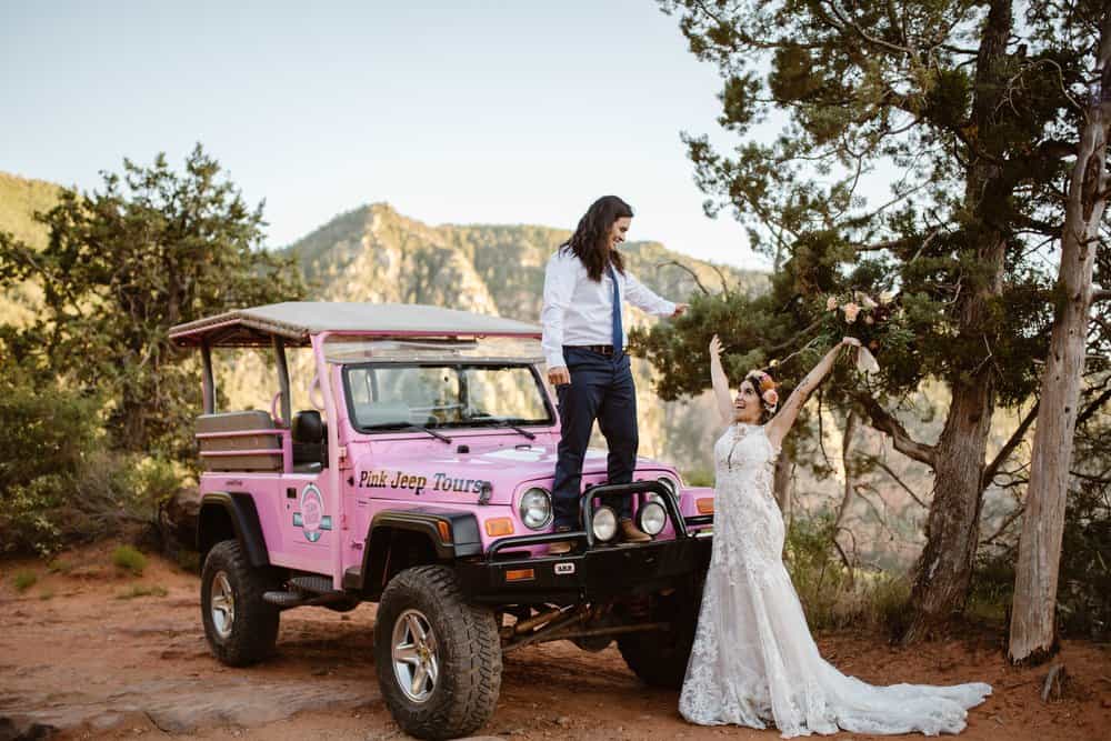 A couple celebrates their marriage while standing on top of a pink jeep.