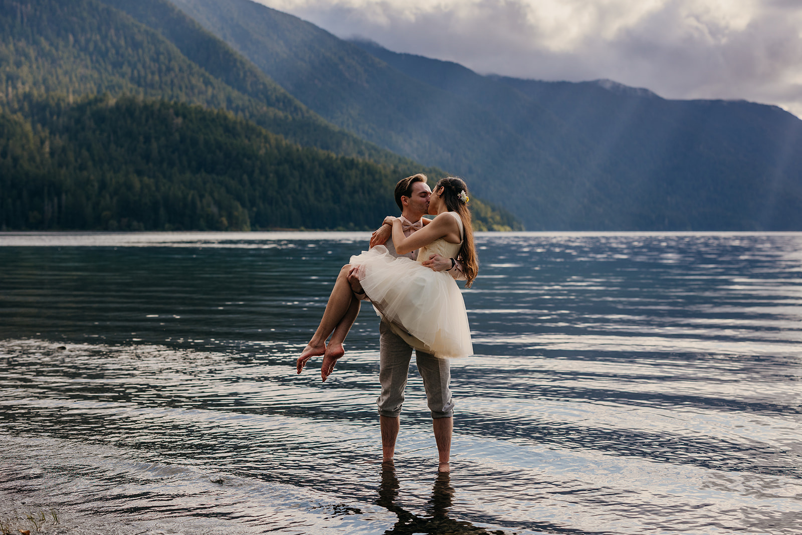 A bride and groom kiss while standing in the lake together.