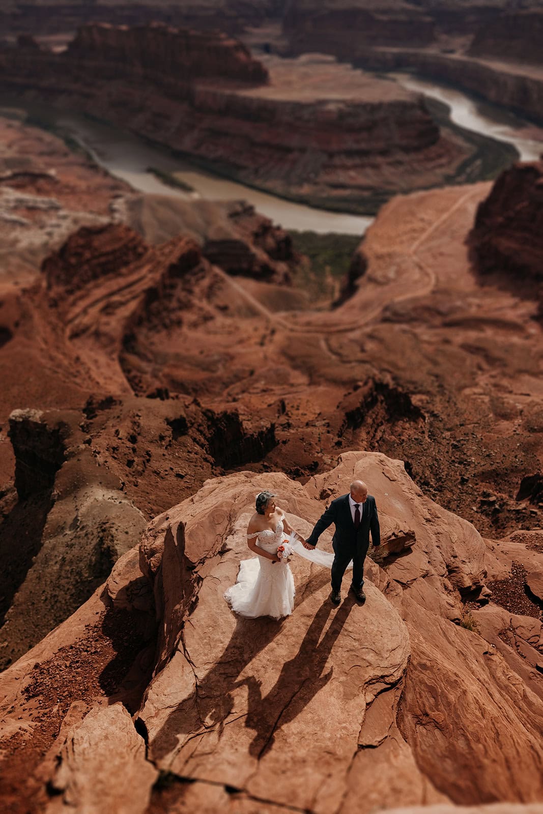 A couple stands in the sun on a cliff for a portrait on their wedding day in Dead Horse Point State Park.