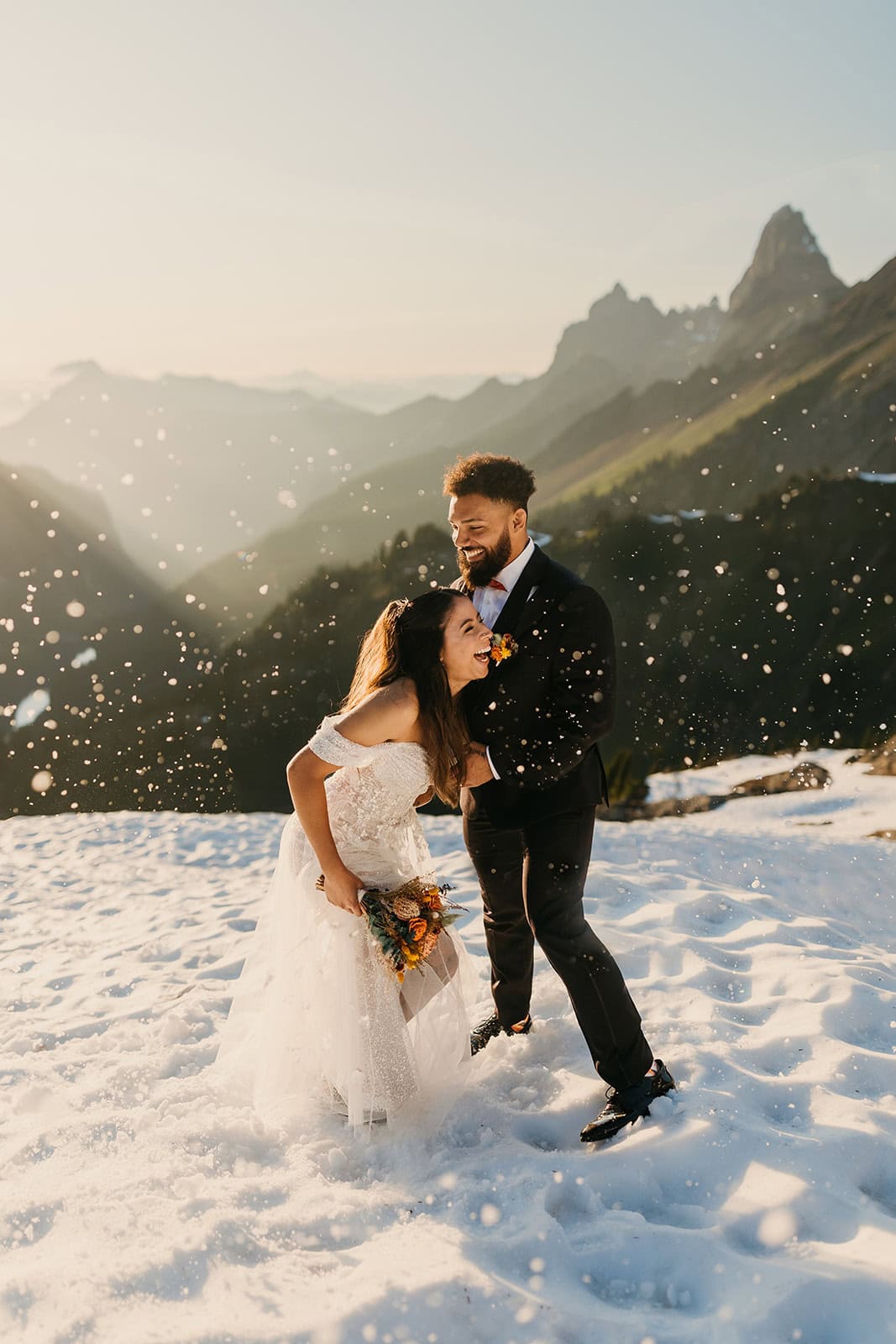 A bride and groom laugh together as they play in the snow following their elopement ceremony in the mountains.