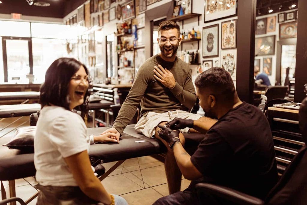 An engaged couple sit together to get a tattoo of their dog.