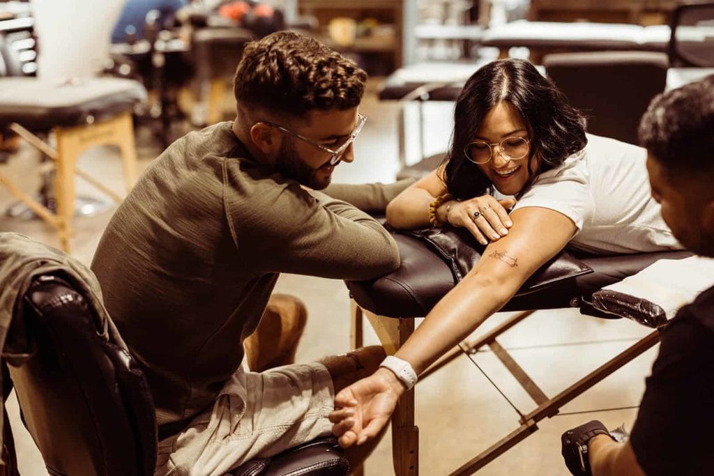 An engaged couple sit together to get a tattoo of their dog.