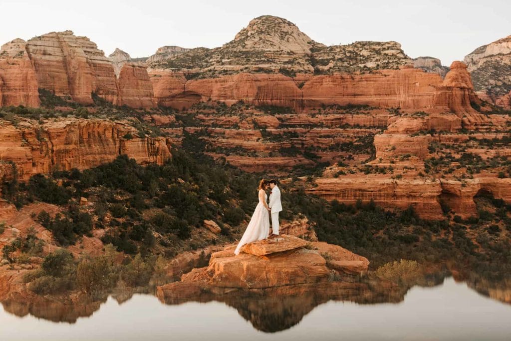 Two brides hold each other close surrounded by red rock canyons.