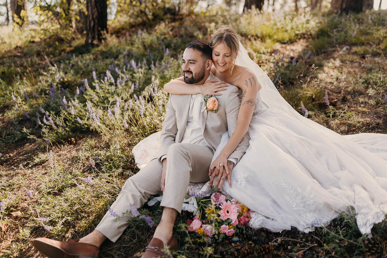 A bride smiles as she holds her groom in a field of flowers.