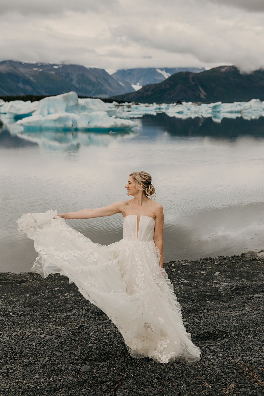 A bride twirls in her Lillian West elopement gown in front of a glacier lake.
