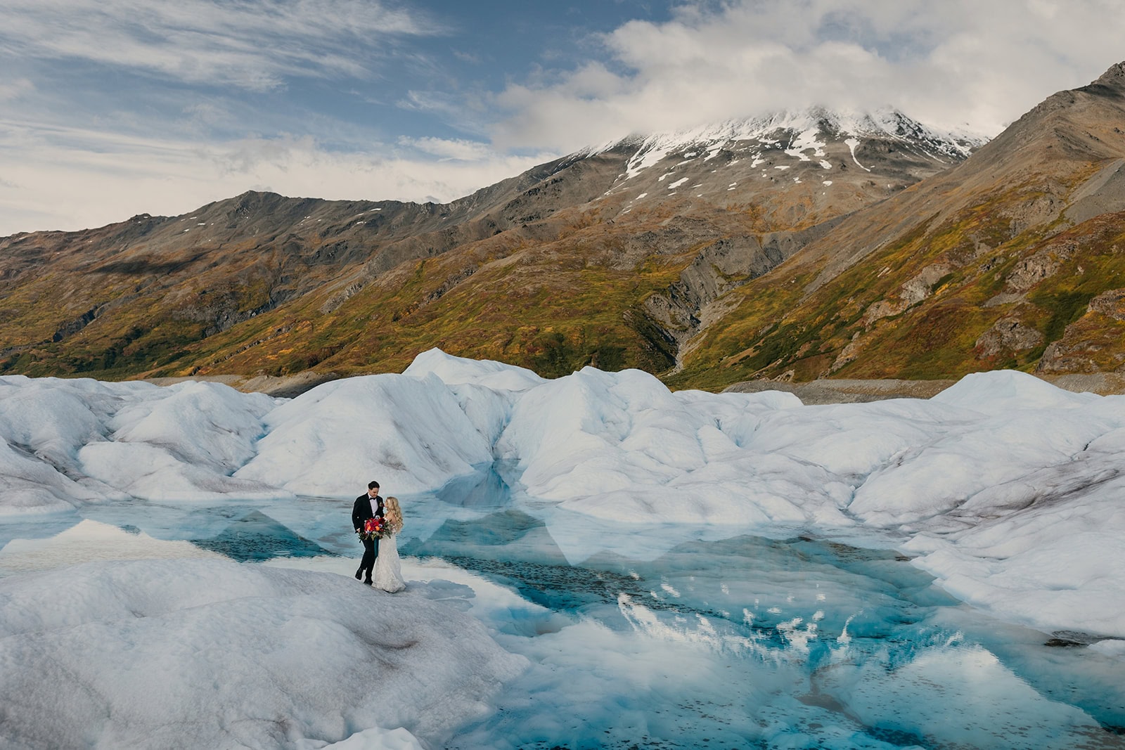 A couple walks across a glacier in the mountains of Alaska.