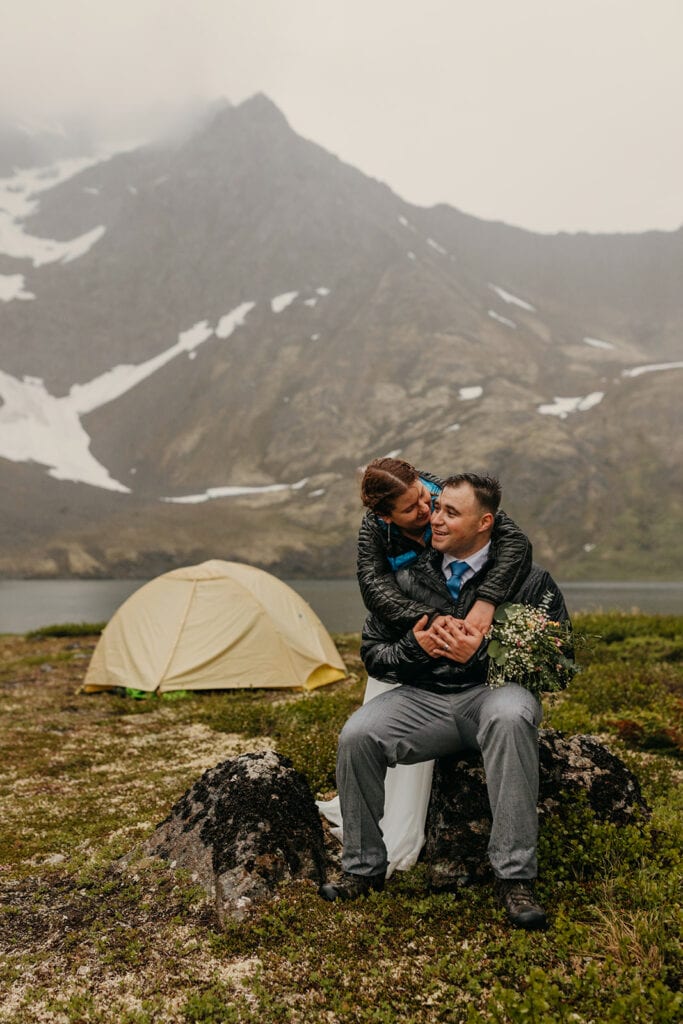 The bride hugs the groom by their tent as he smiles.