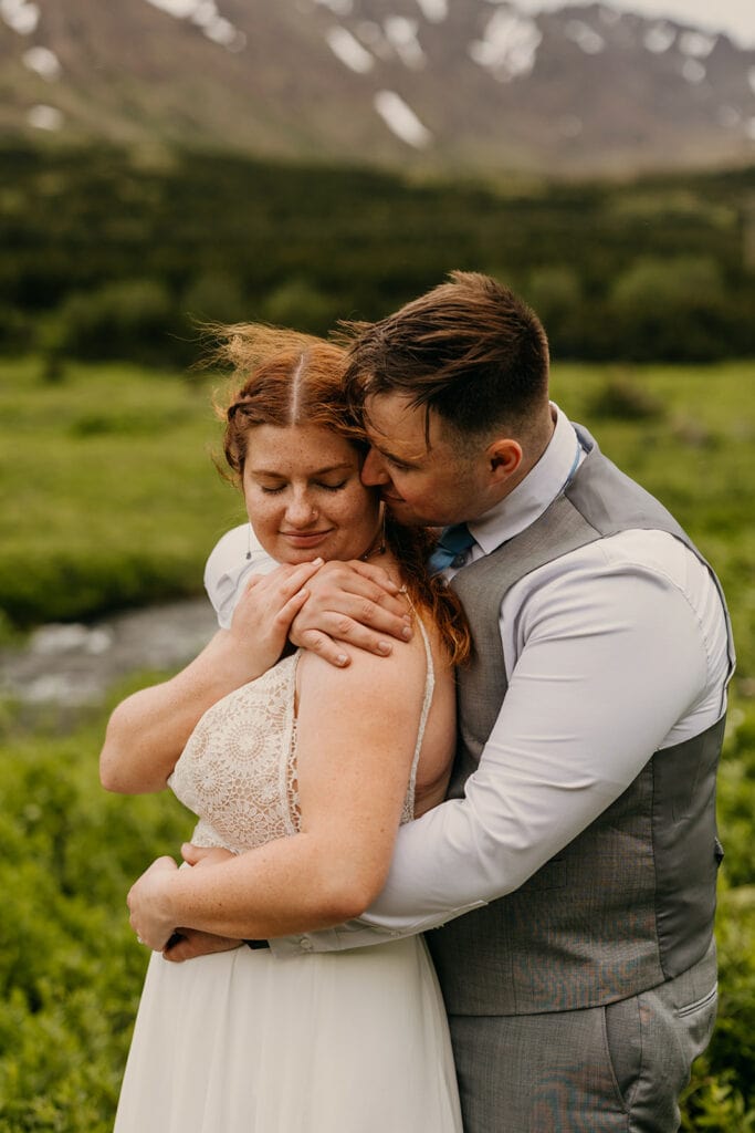 The groom wraps up the bride and kisses her cheek.