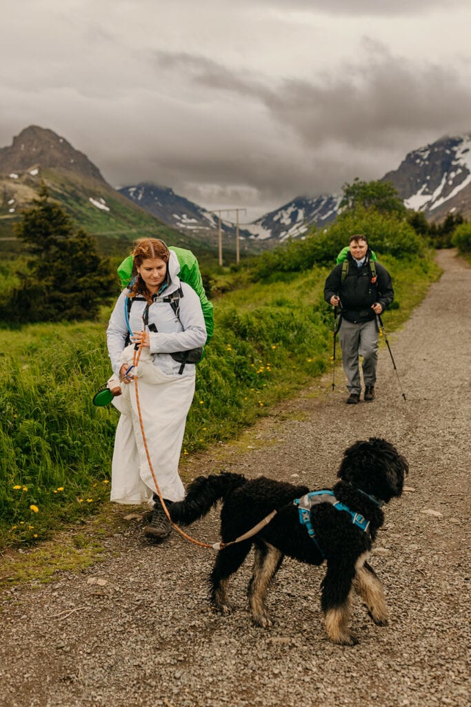 The bride and groom hike along the trail with their dog.