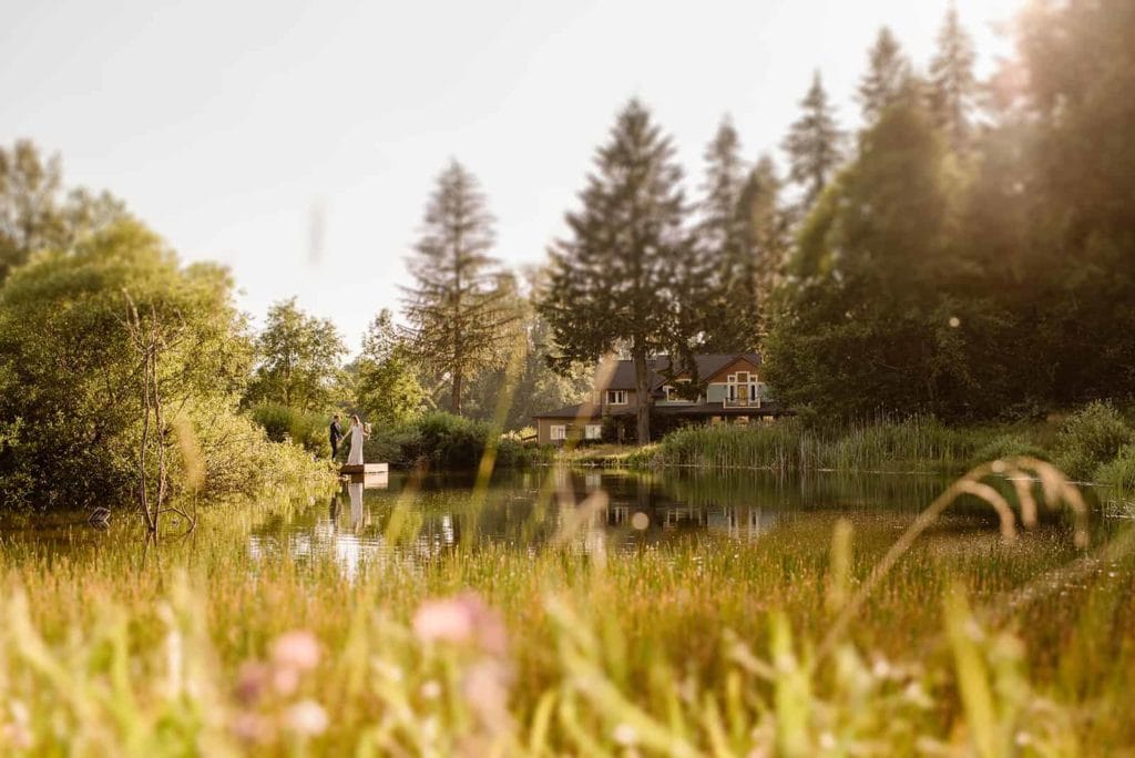 A bride and groom stand together on a dock of a private pond.