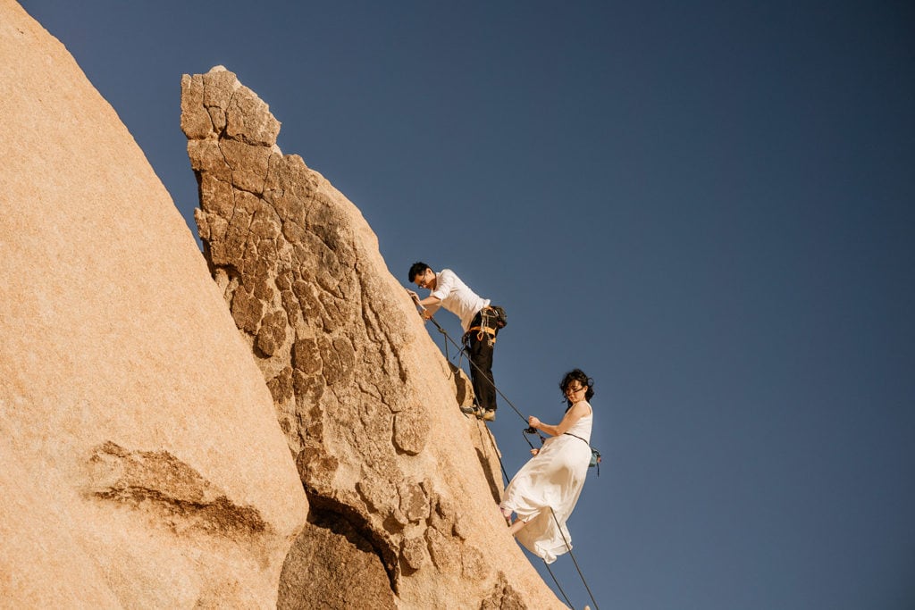 A couple raps down a climbing route together in their wedding attire.