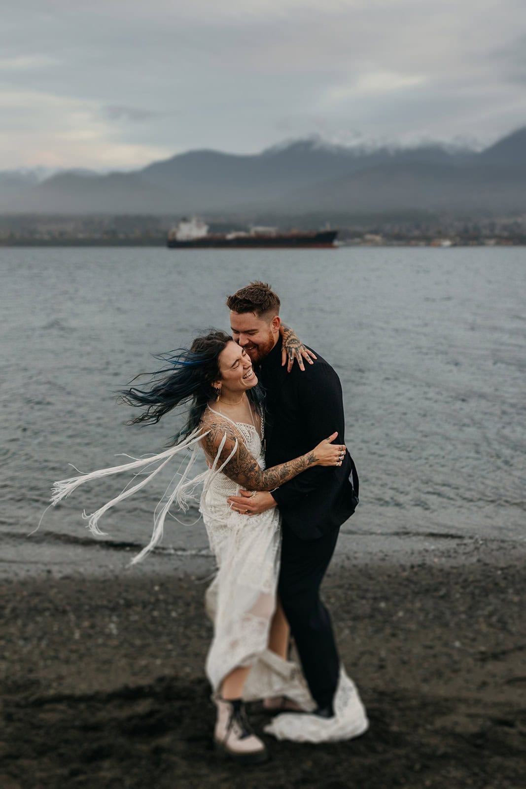 A bride and groom embrace closely in laughter on the beach while eloping.