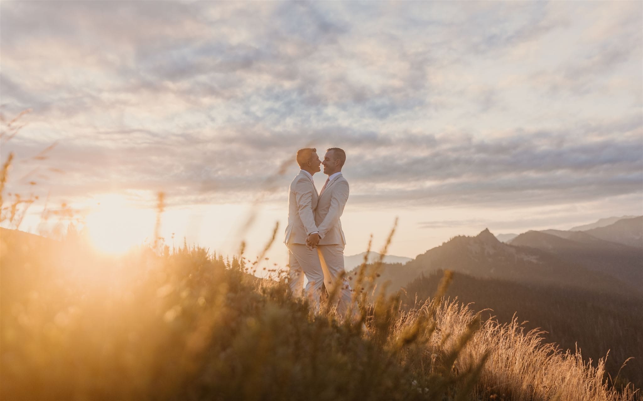 Two grooms kiss in the morning light in the mountains to start off their elopement.