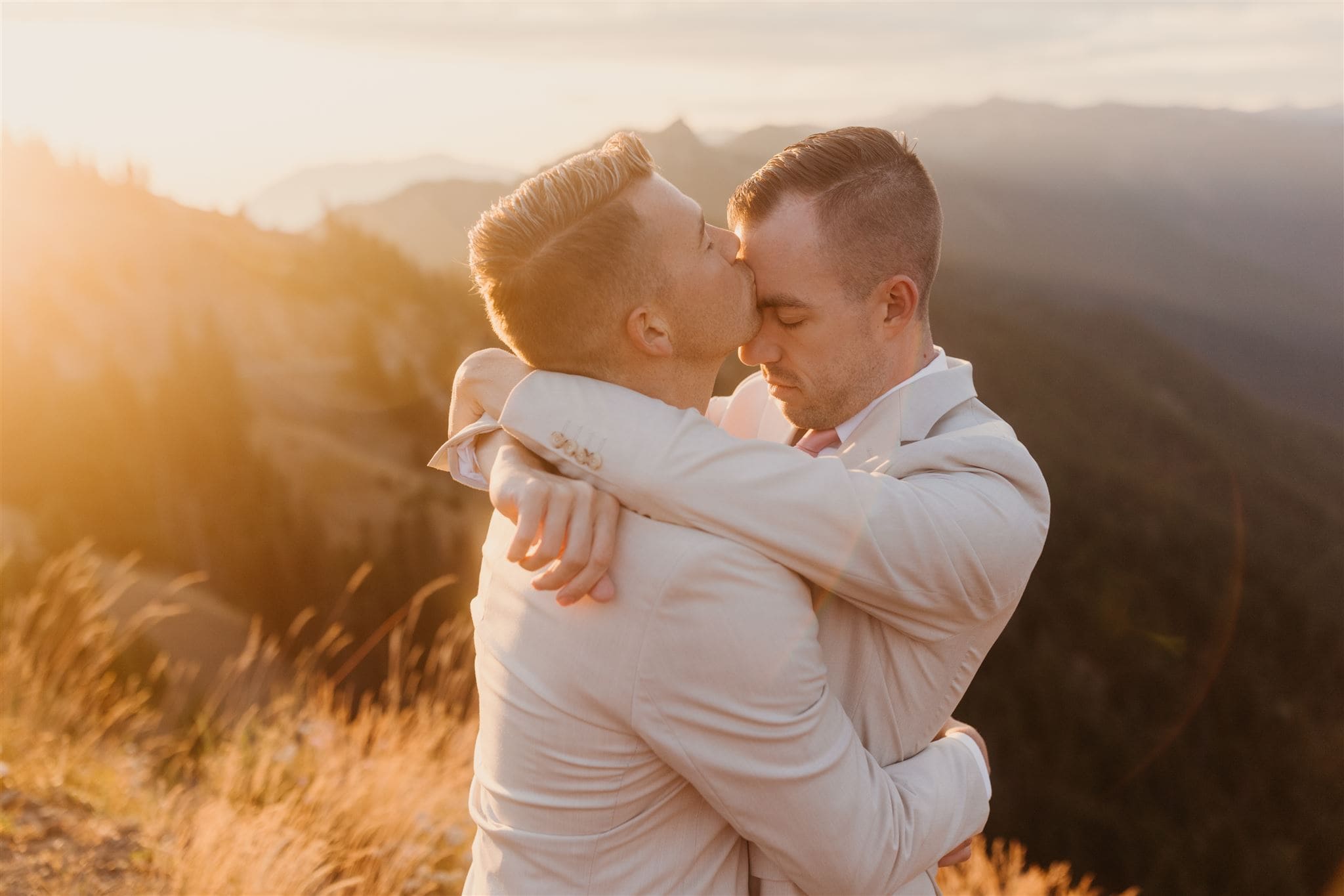 Two grooms hold each other close in the morning light in the mountains.