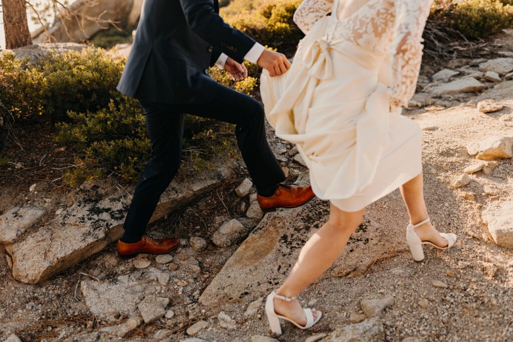 The bride and groom walk together on rocks to their ceremony. 