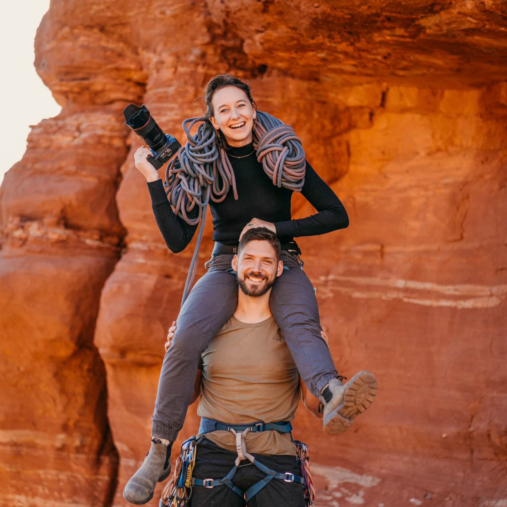 a man holding a woman on his shoulders who herself is holding a camera