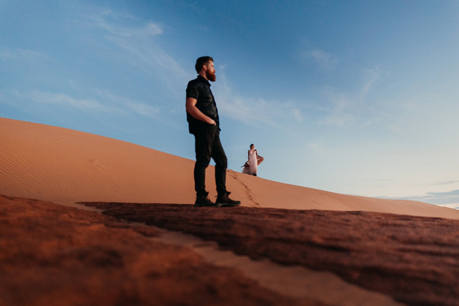A couple stands in the sand dunes watching sunset in Moab