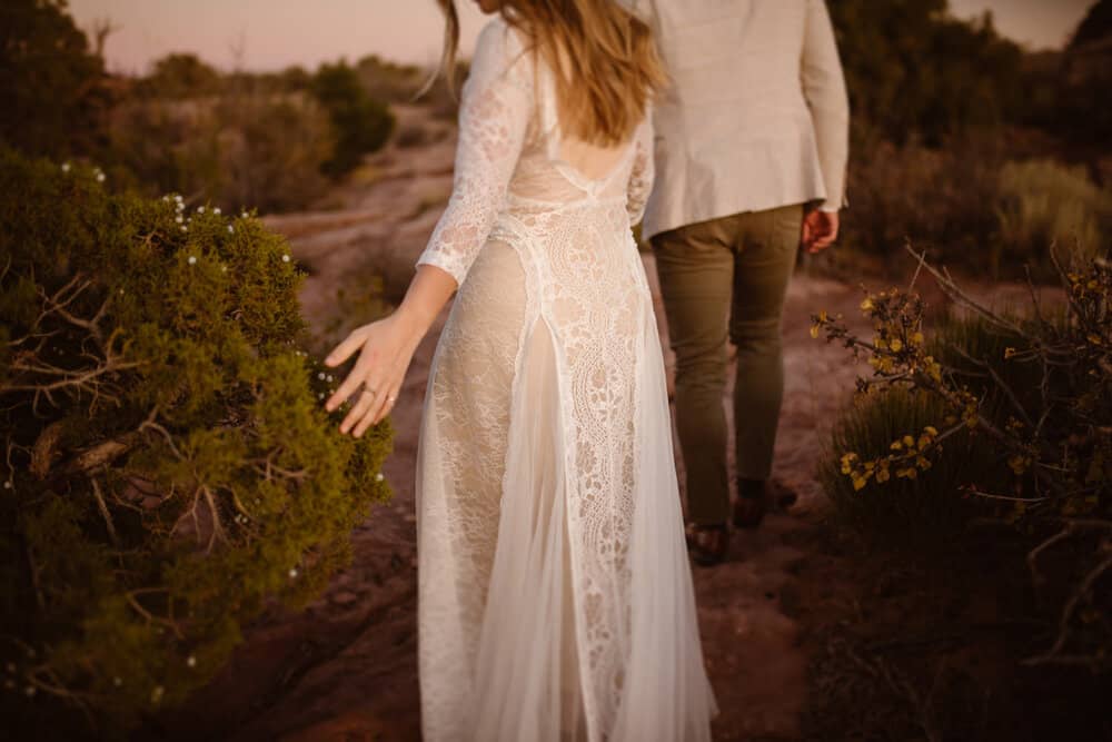 A bride touches a bush as she walks by it.