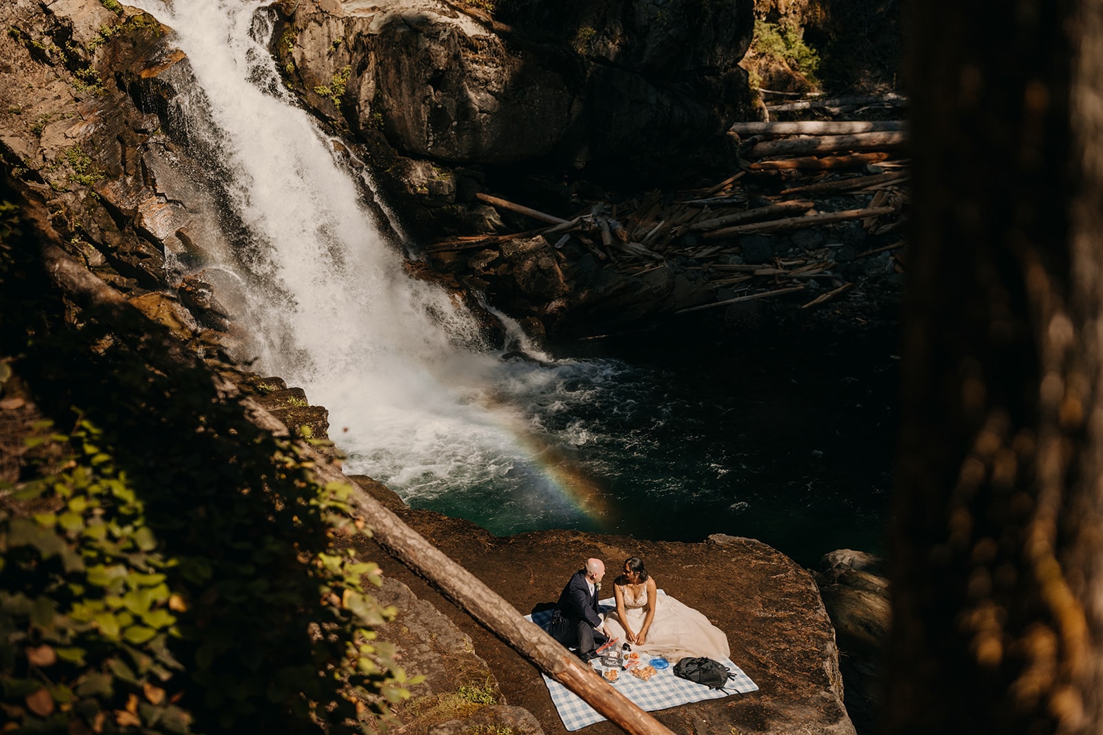 A couple sits together at a waterfall having a picnic.