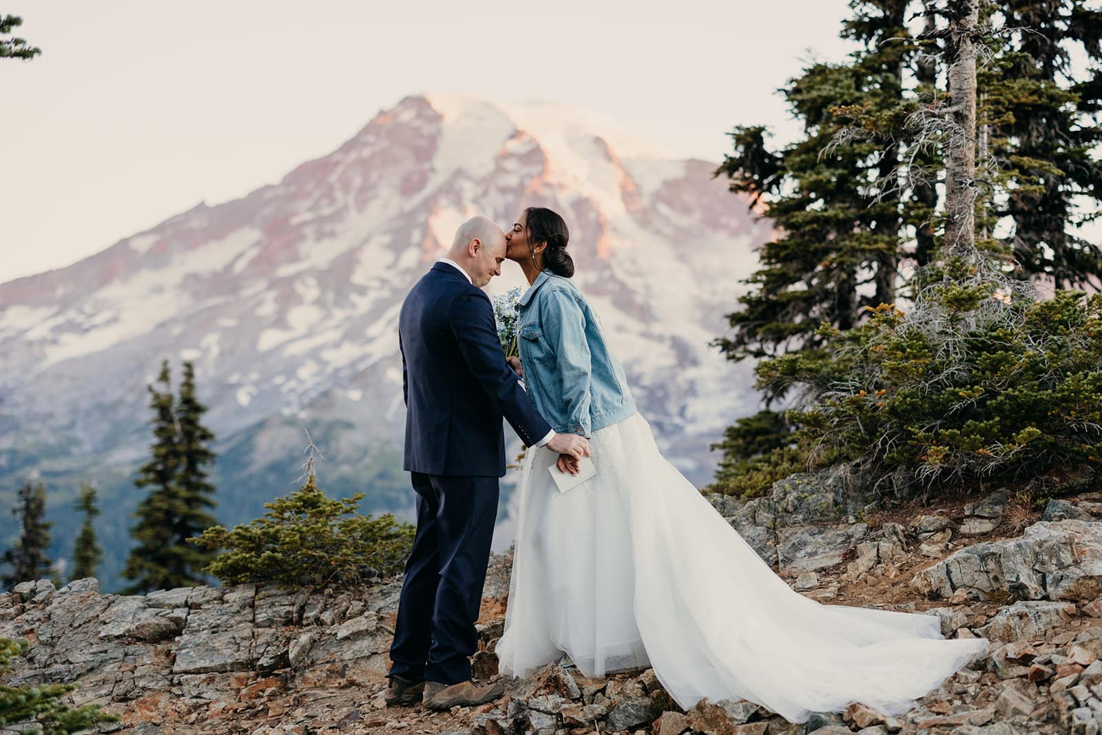 A groom is taken with emotion as his bride gives him a kiss on the forehead.