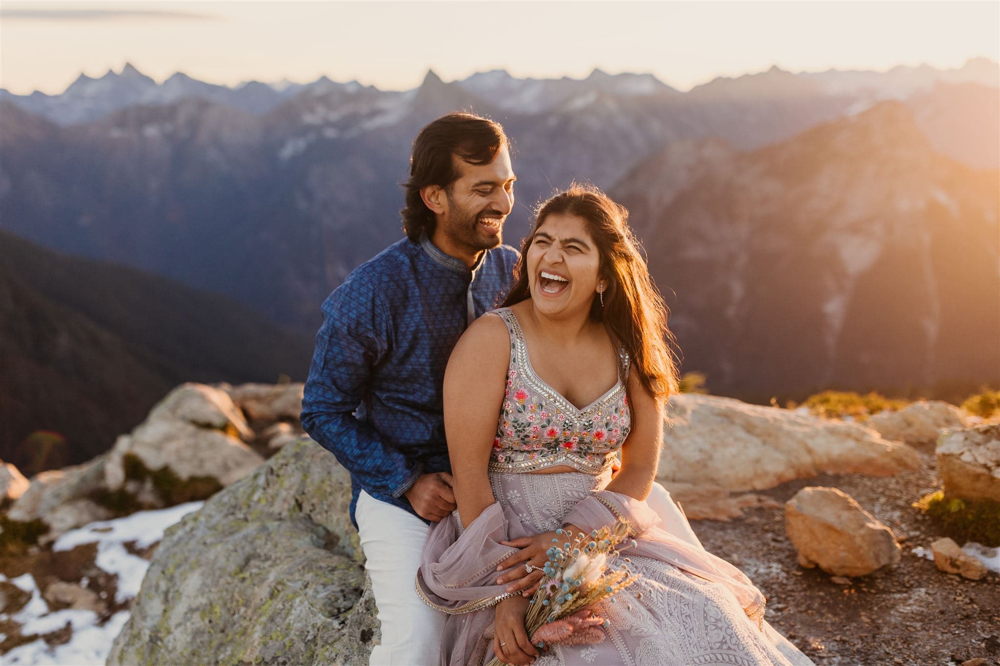 A couple laughs together in the sunrise light in the mountains.