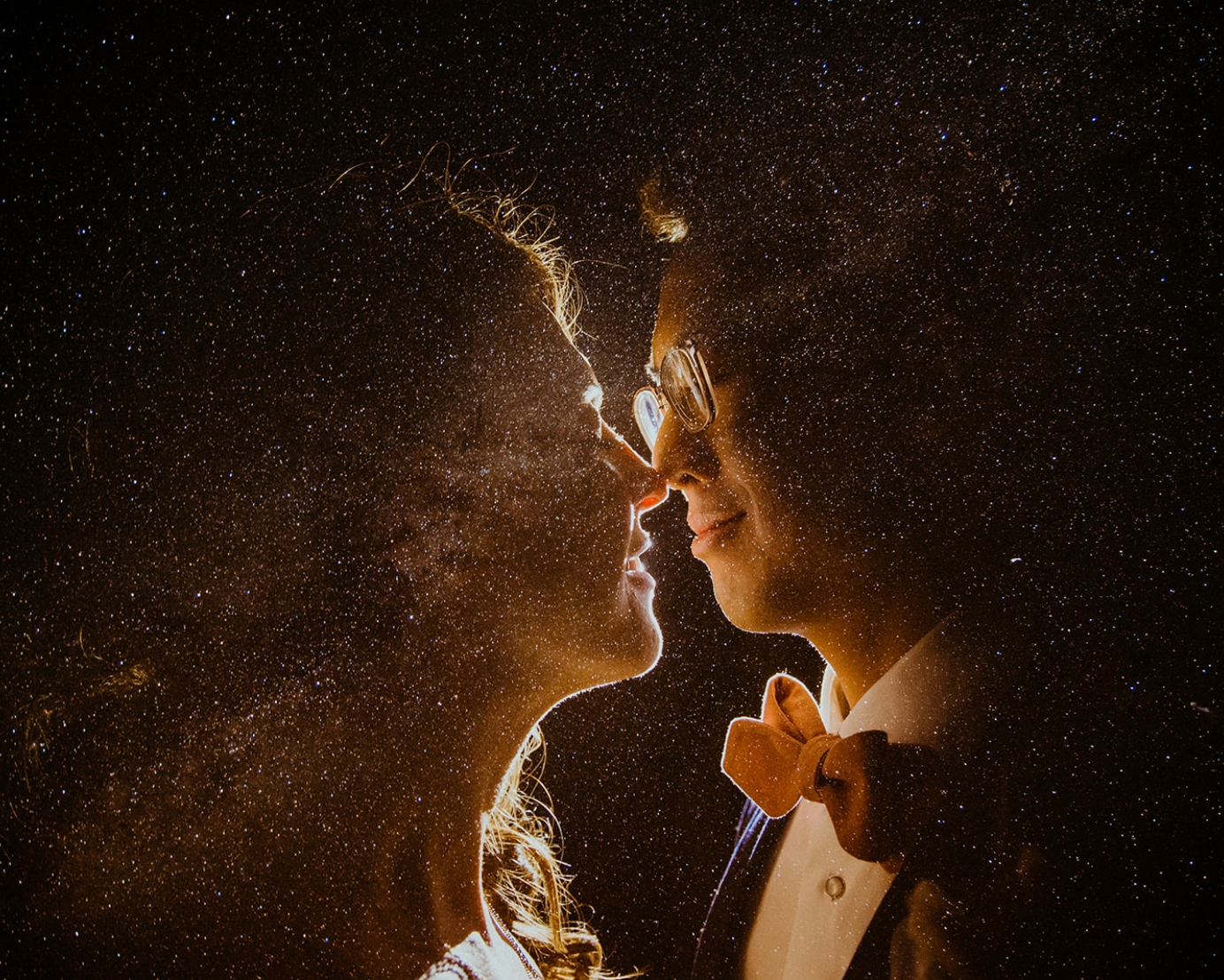 Two partners lean in for a kiss with the night sky overlaid around them.
