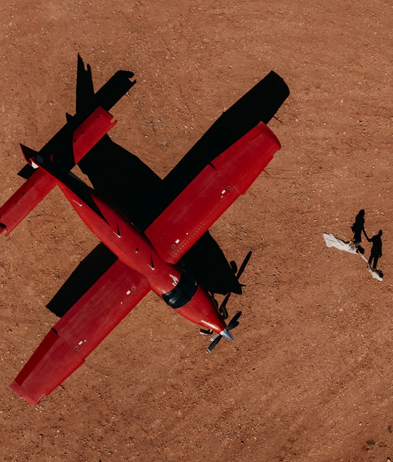 Aerial view of a red plane and a couple standing with their shadows in Moab.