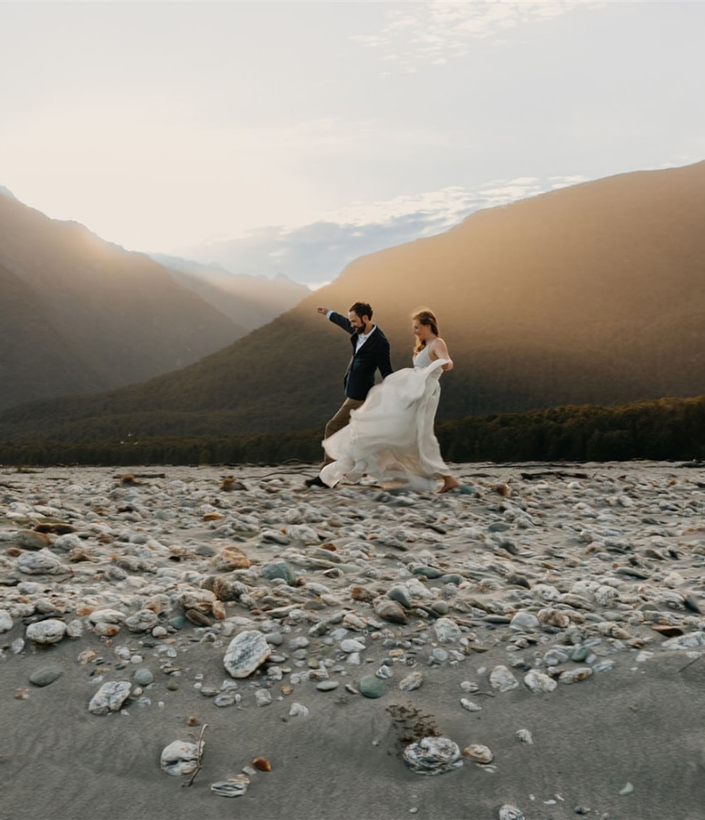 Two couples run and hold hands in New Zealand surrounded by mountains.