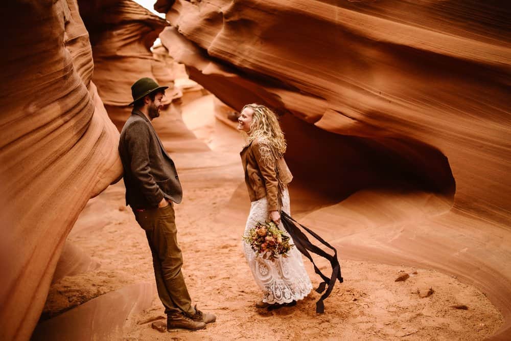 A groom smiles at his bride as she runs towards him in a slot canyon.