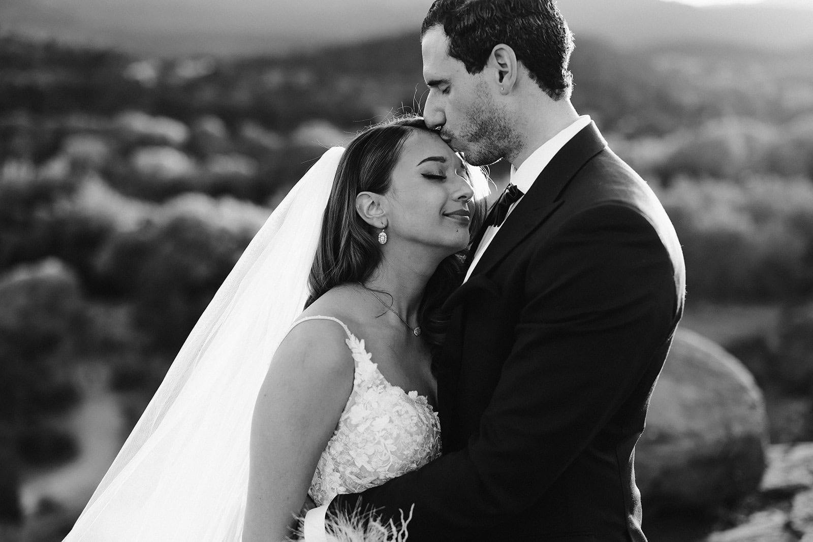 A bride gets a forehead kiss from her groom with her eyes closed.