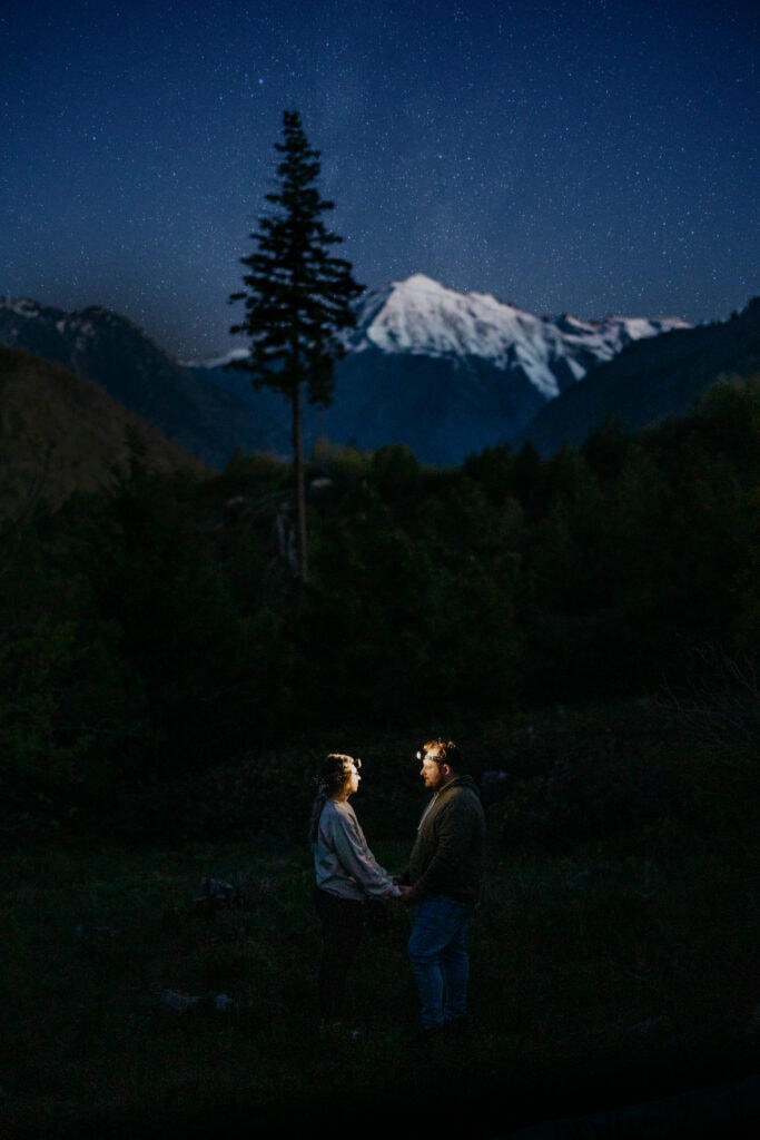 A couple holds hands under the stars and the mountains. 
