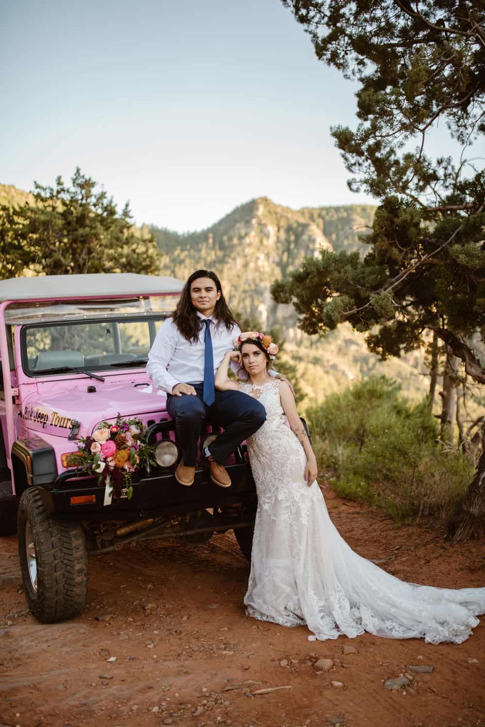 A bride and groom stand for a portrait in front of the jeep.