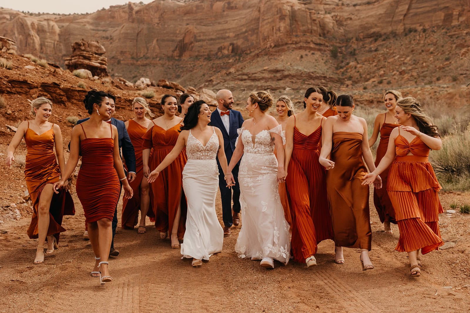 Two brides walk in the desert with their bridal party.