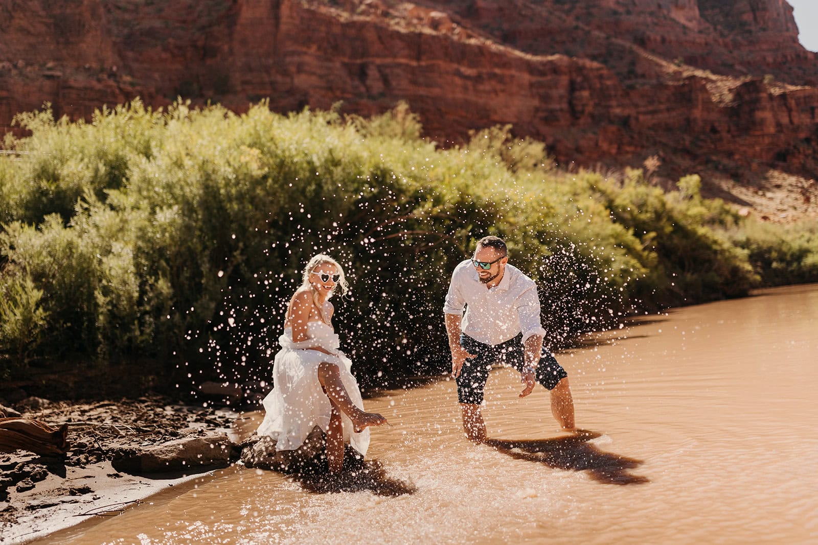 A couple splash in the Colorado River together on a sunny day in Moab.