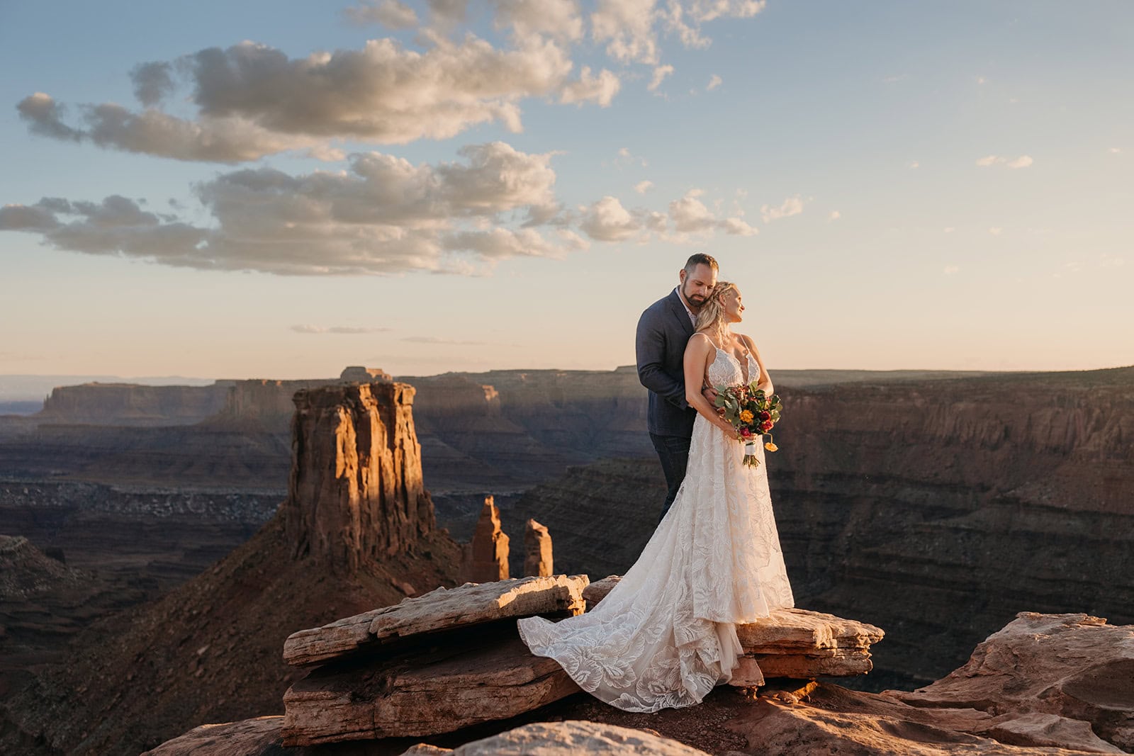 A groom holds his bride at sunset showcasing her dress. 
