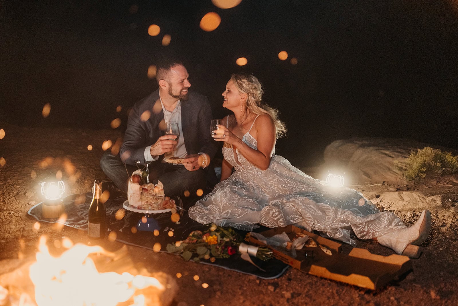 A couple sits by a fire and eat their wedding cake out on BLM land in Moab