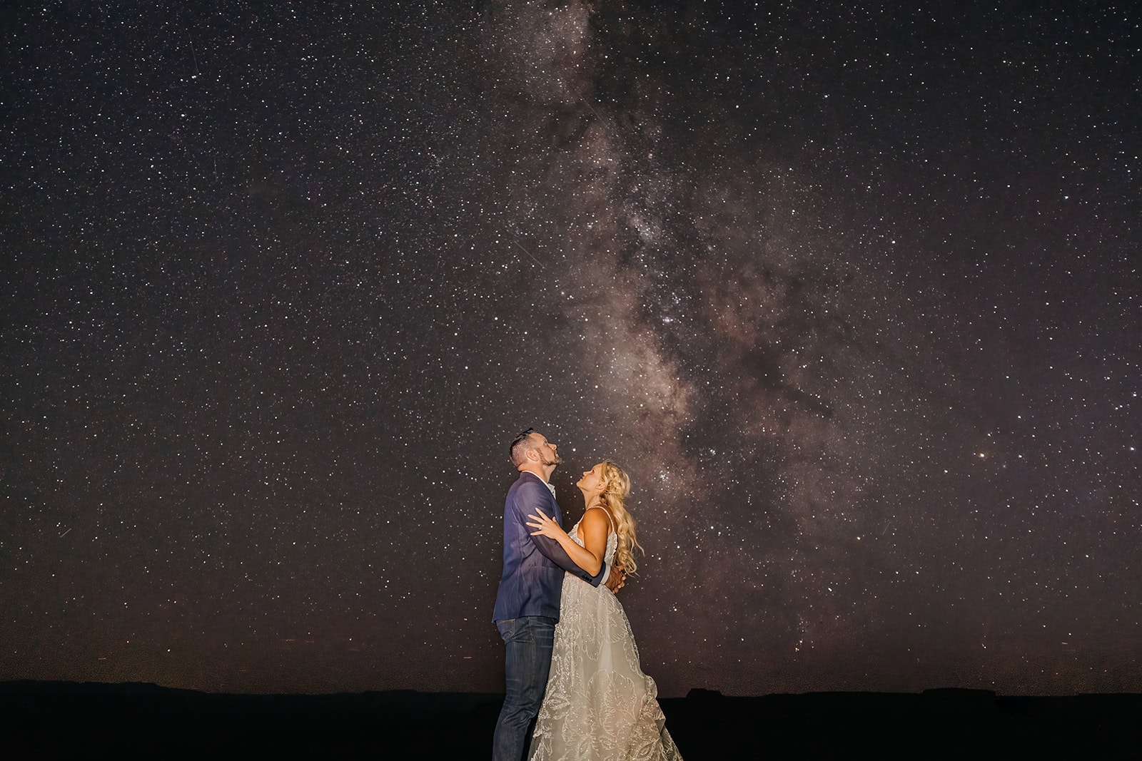 A couple holds each other as they look up towards the sky admiring the milky way on a fall evening in Moab.