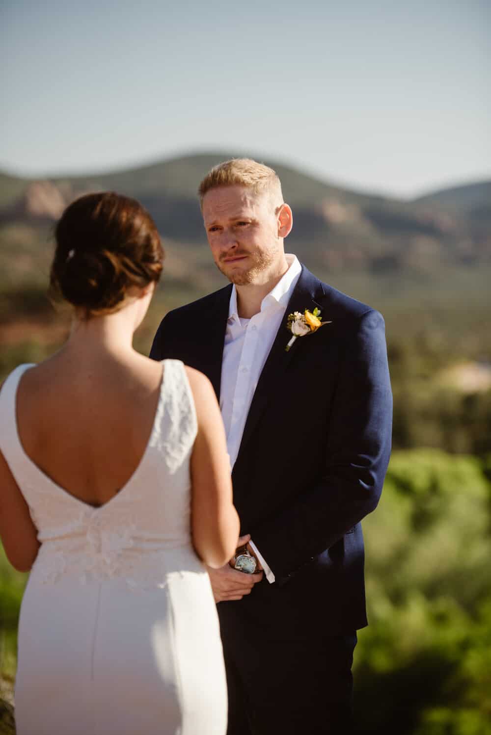 The groom smiles as the bride shares her vows. 