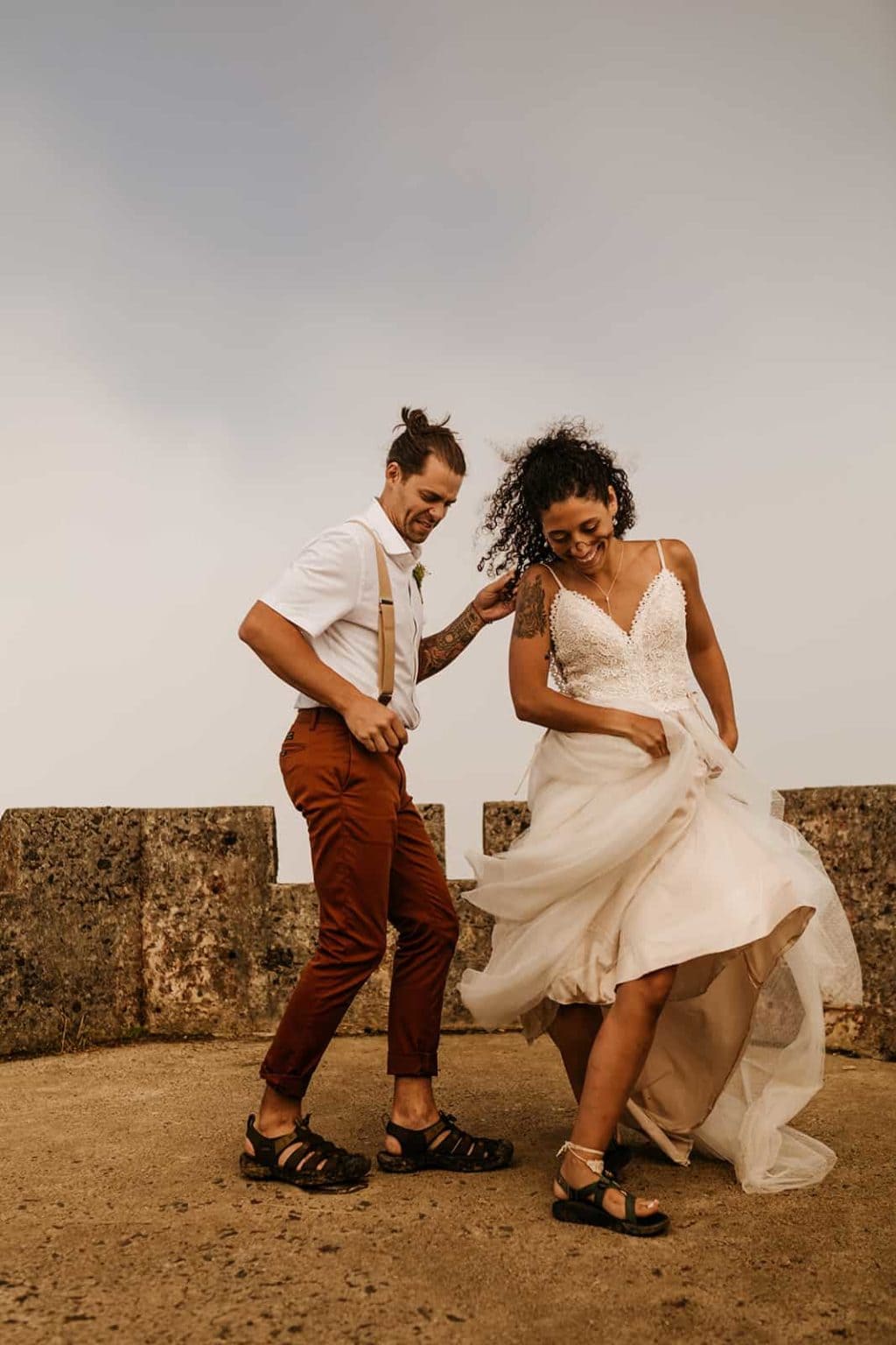 A bride and groom dance together in their keens and chacos on top of a mountain tower in the rainforest.