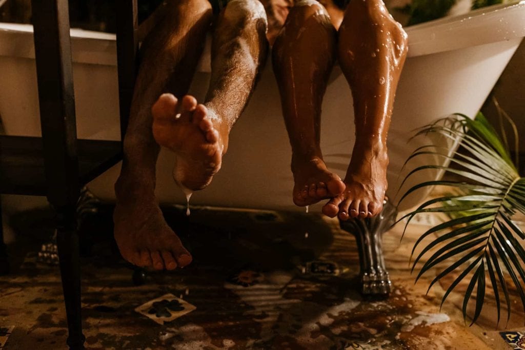 A couples feet hanging out of the tub as water drops off of them.