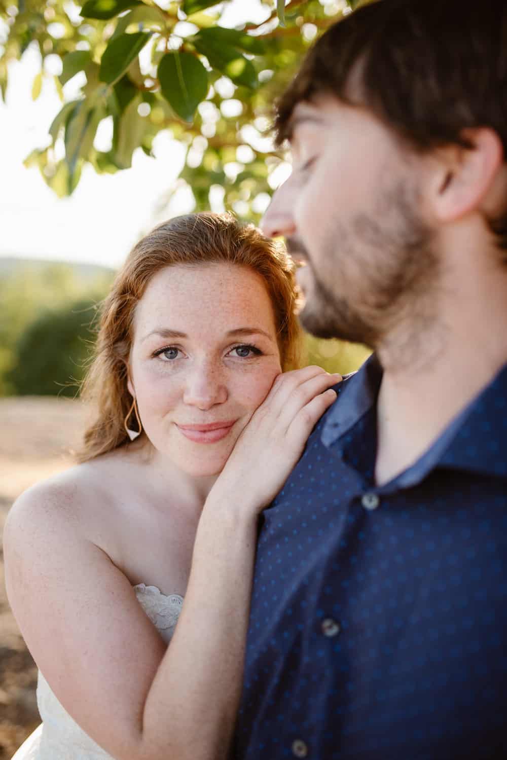A bride looks at the camera as she leans onto her groom.