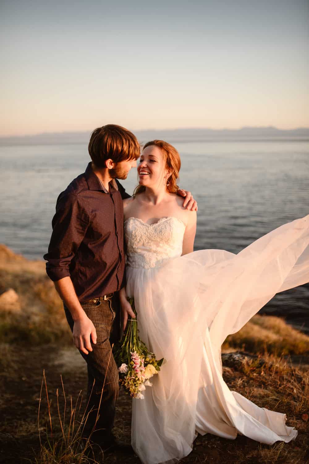 A bride throws her dress into the wind while looking at her husband.