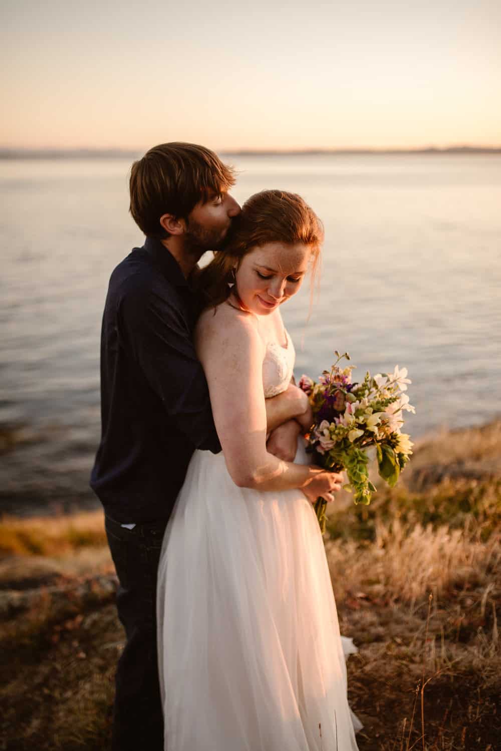 A man holds and kisses his wife as she holds her flowers.