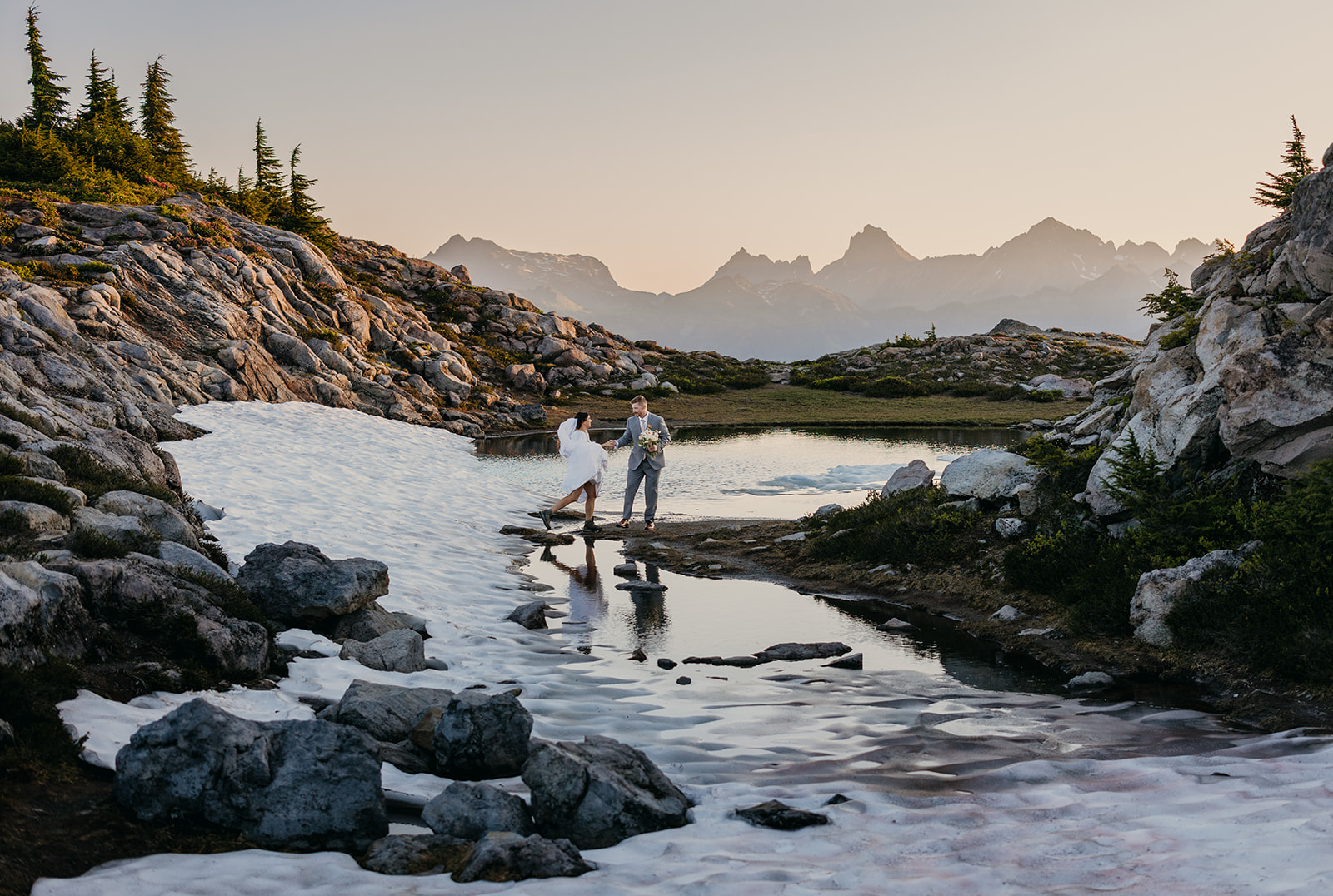 A groom leads his bride across the snow melt at Huntoon Point.