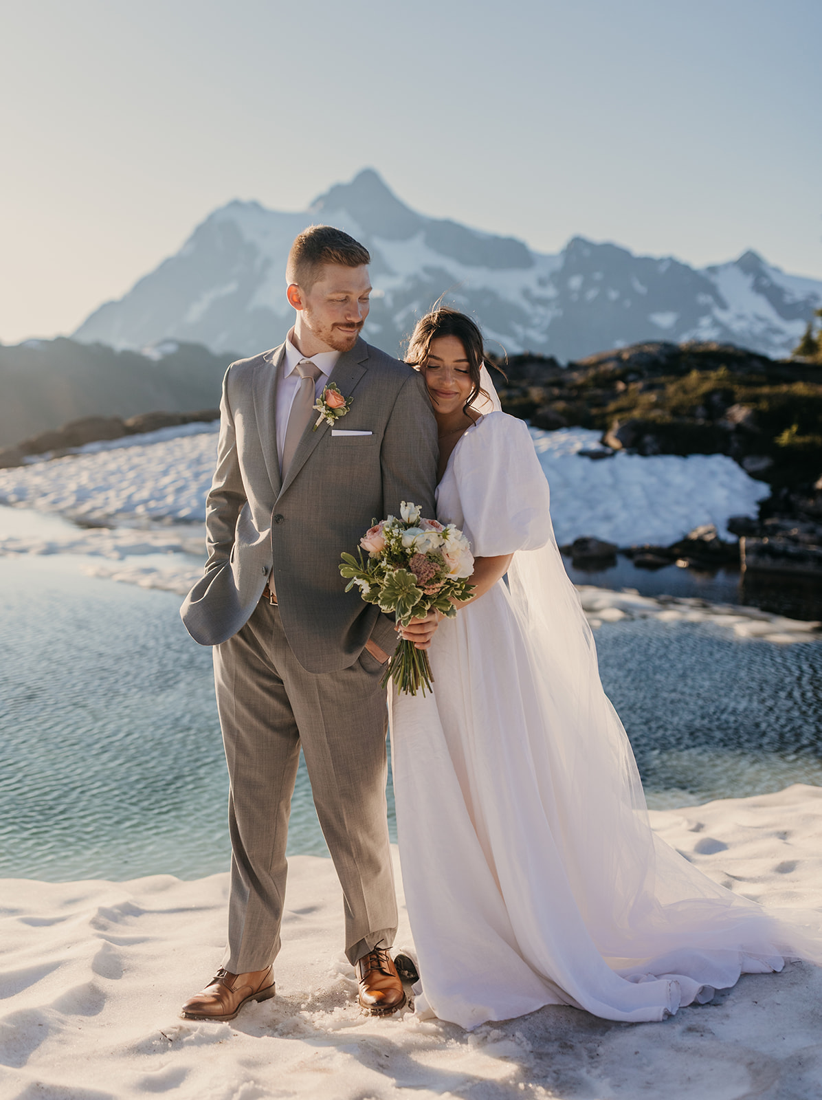 A bride stands with her husband for a close moment on the snow at sunrise.