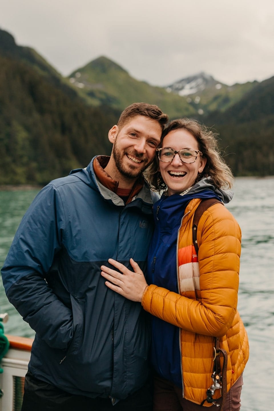 a man and woman stand together wearing rain gear while out on a boat.