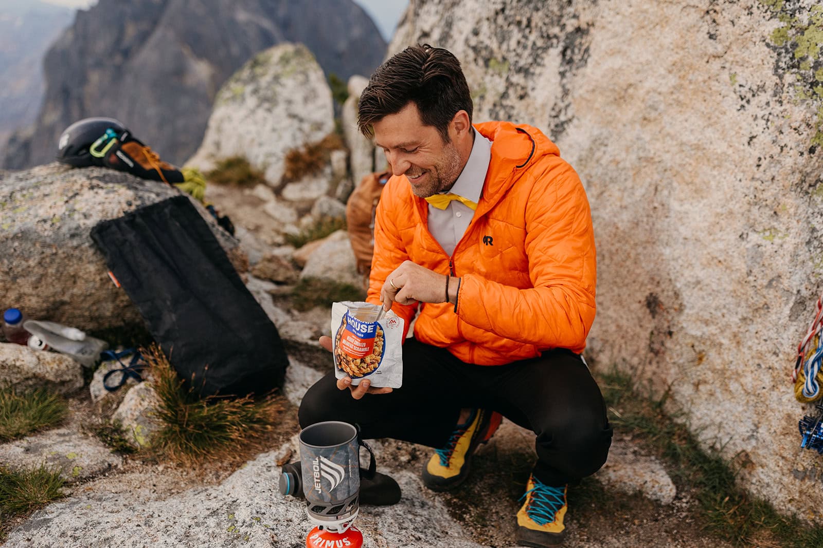 A man wearing an orange jacket making a meal with a jet boil